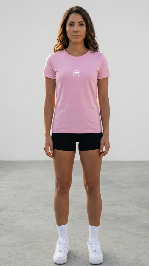 A woman stands facing forward in a studio wearing a light pink short-sleeve t-shirt with a small white circular GP logo on the chest, black athletic shorts, white socks, and white sneakers.