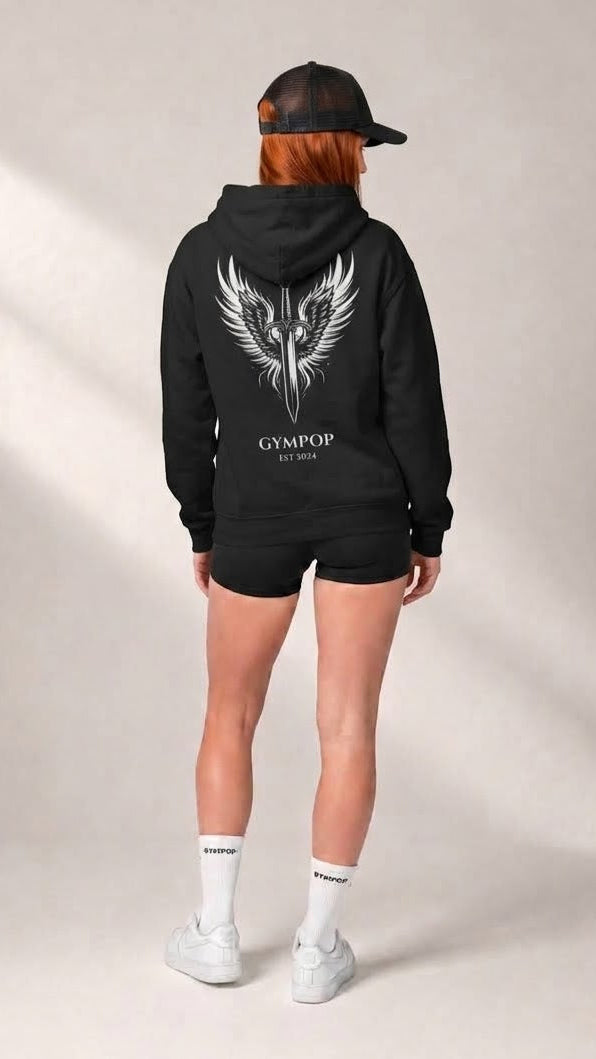 A model shown from the back wearing a black hoodie with a large white winged dagger graphic and the text 'GYMPOP EST. 2025' on the back, paired with black shorts, white socks, and white sneakers against a neutral studio backdrop.