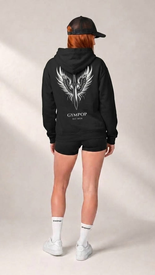 A model shown from the back wearing a black hoodie with a large white winged dagger graphic and the text 'GYMPOP EST. 2025' on the back, paired with black shorts, white socks, and white sneakers against a neutral studio backdrop.