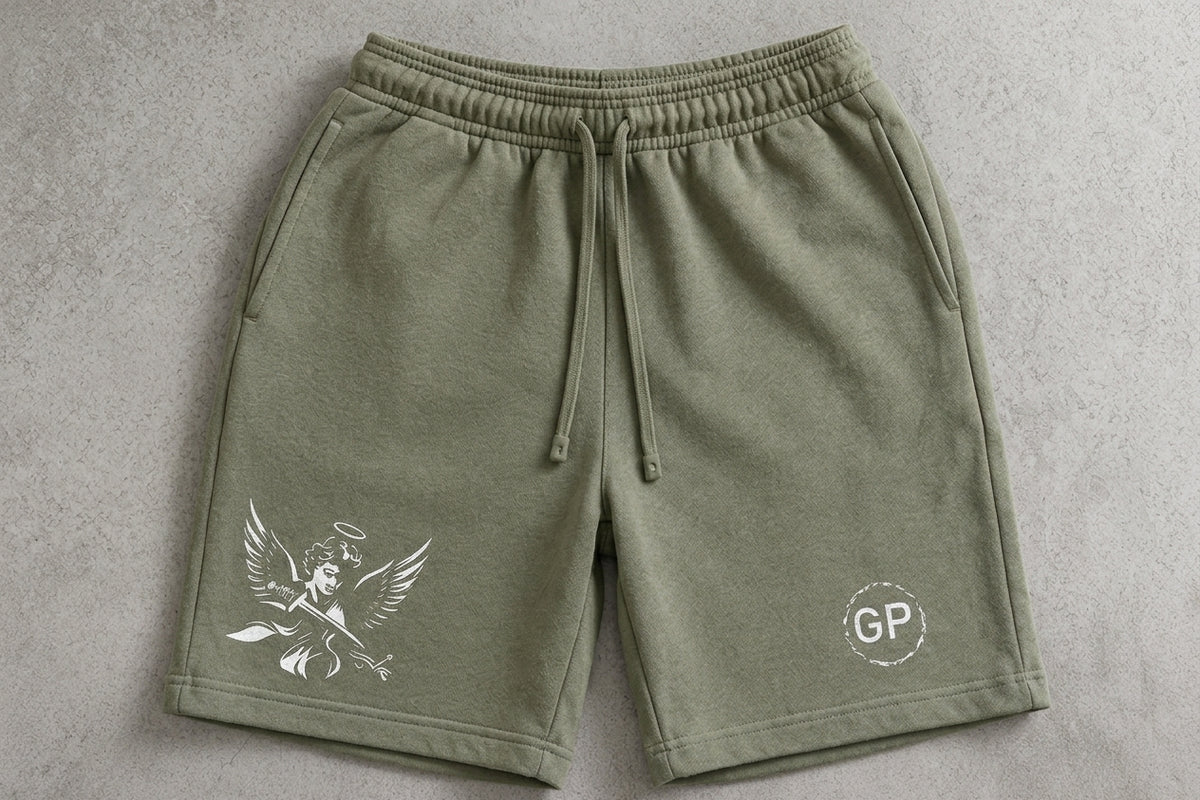 Olive green sweat shorts with a white graphic of a winged figure on the left leg and a circular 'GP' logo on the right leg, laid flat on a gray textured background.