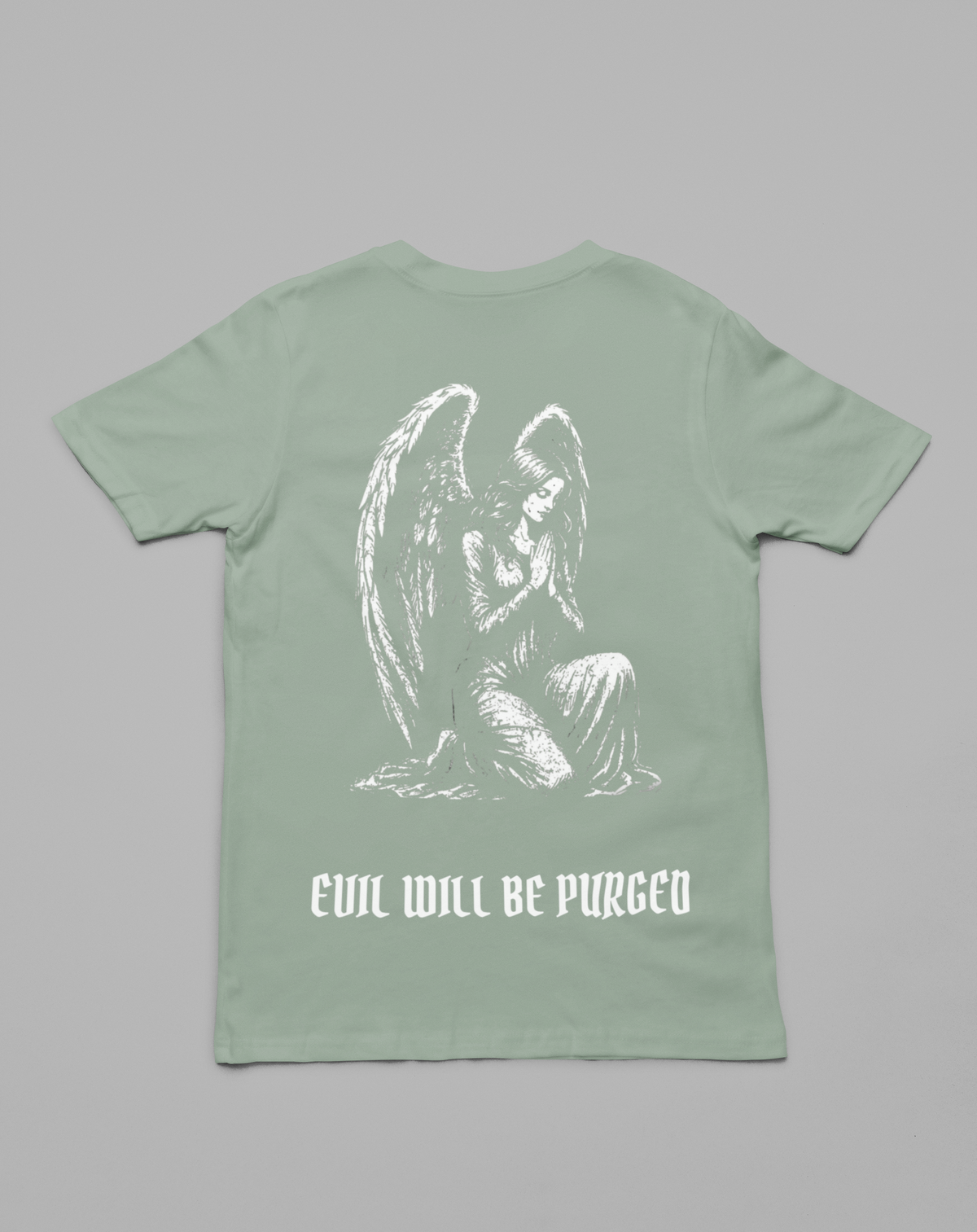 A sage green short-sleeve t-shirt shown from the back, featuring a white sketch-style graphic of a kneeling angel and the text 'EVIL WILL BE PURGED' printed below it, set against a solid gray background.