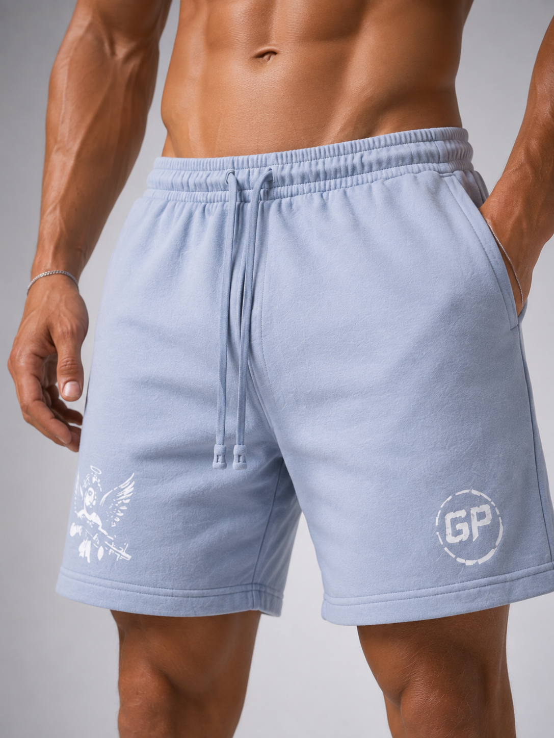 A close-up of a man wearing light blue drawstring shorts with white printed Gympop logos on the left and right legs, shown against a neutral grey studio background.