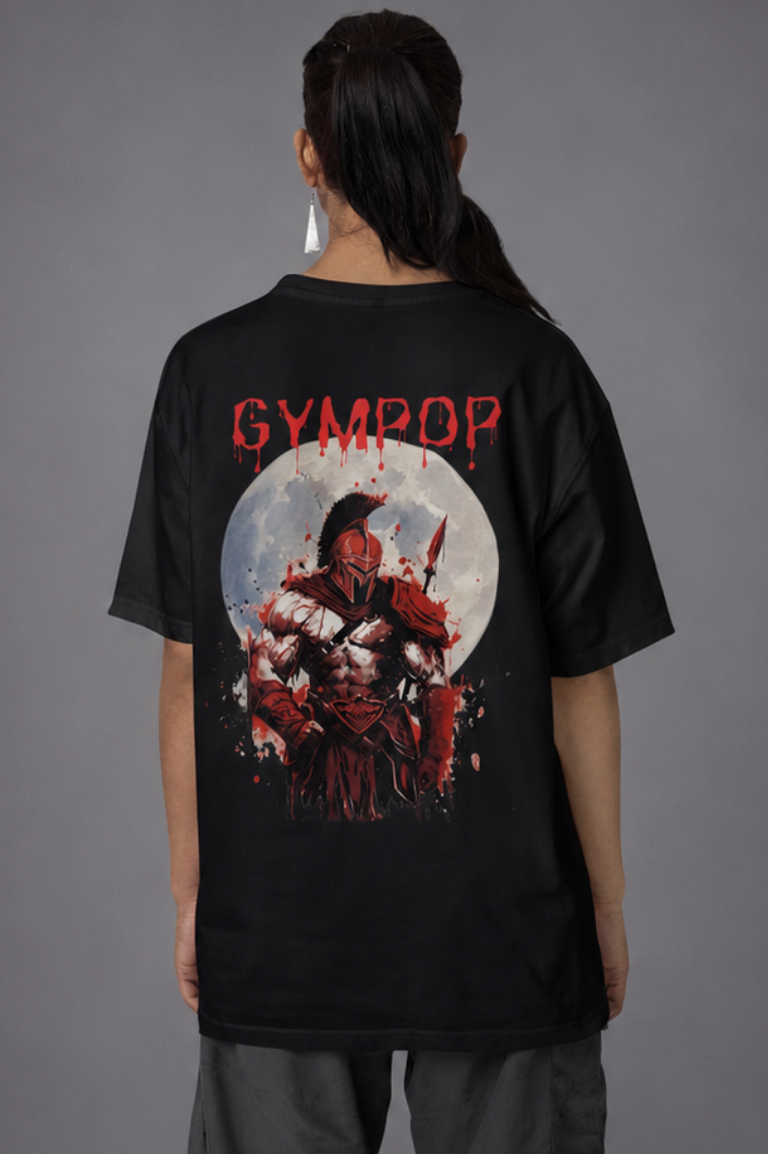 A person shown from the back wearing a black oversized T-shirt with a large red and white Spartan graphic print and the word 'GYMPOP' across the upper back, paired with loose dark grey pants and white sneakers against a grey studio background.